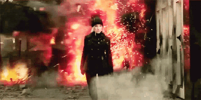 a woman in a black coat is standing in front of a fire .