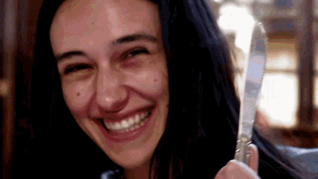 a woman is holding a knife and smiling for the camera