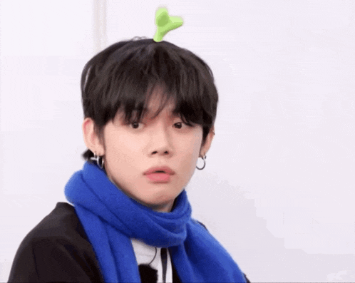 a young man with a green plant on his head is wearing a blue scarf and earrings .