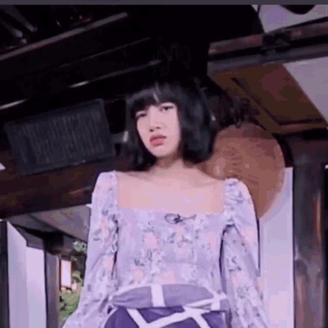 a woman in a purple floral top and purple skirt is standing in front of a wooden door .