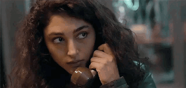 a woman with curly hair is talking on a telephone and looking at the camera .