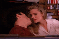 a man and a woman are kissing in front of a bookshelf .