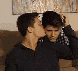 a man is kissing another man on the forehead while sitting on a couch .