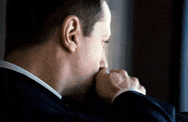 a man in a suit looks out a window with his hand on his face