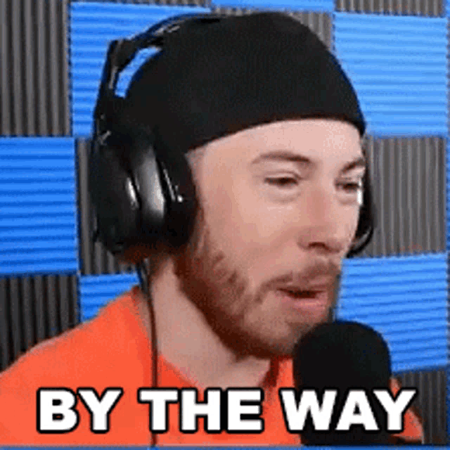 a man wearing headphones and a beanie is talking into a microphone and says `` by the way '' .
