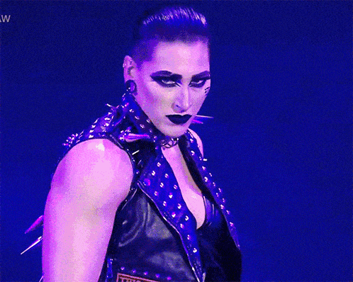 a woman in a leather vest and choker is standing in front of a screen that says ww