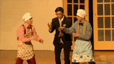 a man in a suit and tie stands between two women in aprons and chef hats