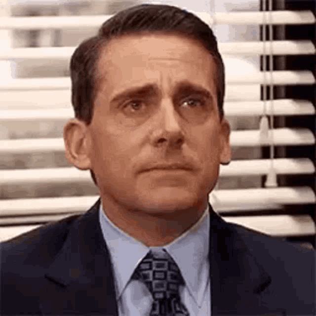 michael scott from the office is wearing a suit and tie and making a funny face .