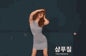a woman in a gray dress is dancing in front of a black wall with chinese writing on it