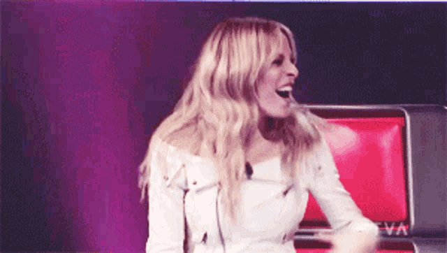 a woman in a white jacket is laughing in front of a tv screen