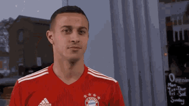 a man wearing a red adidas shirt stands in front of a sign