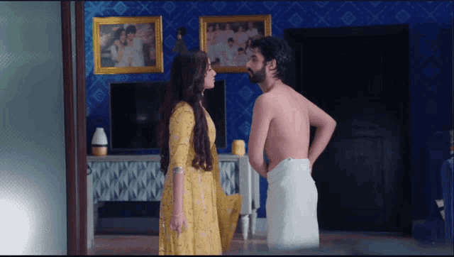 a man in a towel stands next to a woman in a yellow dress in a living room