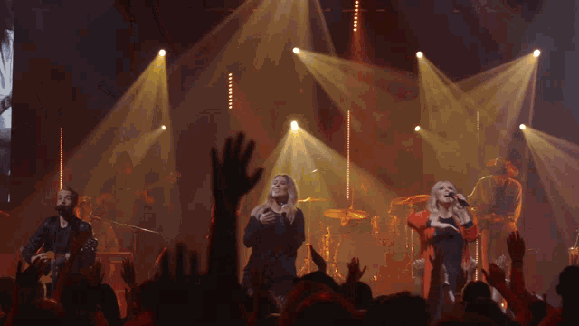a group of people singing on a stage with a crowd watching