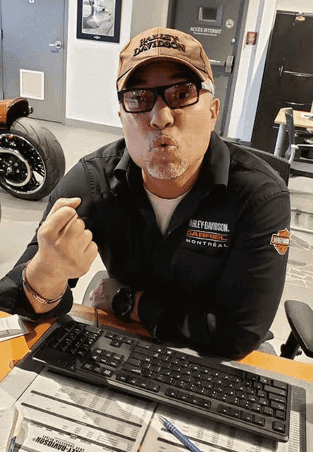 a man wearing a hat that says harley davidson is sitting at a desk