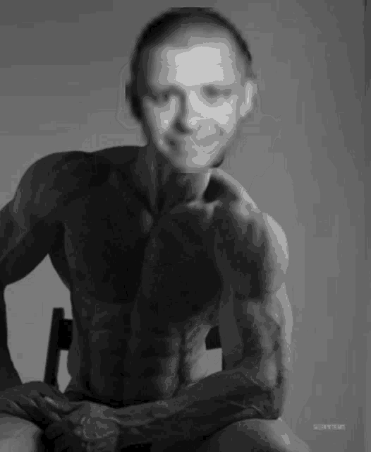 a man without a shirt is sitting in a chair in a black and white photo