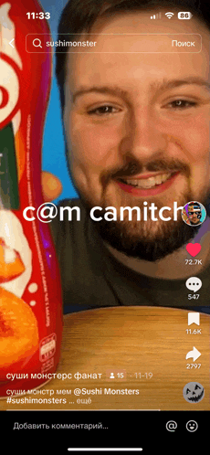 a man with a beard is smiling and holding a bottle of com camitch