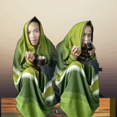 two people wrapped in green blankets are drinking coffee