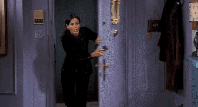 a woman in a black suit is standing in a doorway holding a door knob .
