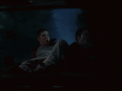 two men are laying on the ground with their mouths open in a dark room