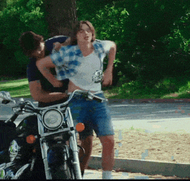 a man is holding another man 's waist while riding a motorcycle
