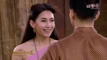 a man and a woman are looking at each other and smiling . the woman is wearing a pink dress .