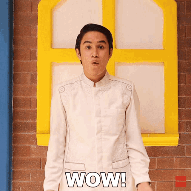 a man in a white shirt is standing in front of a yellow window and the word wow is on the screen