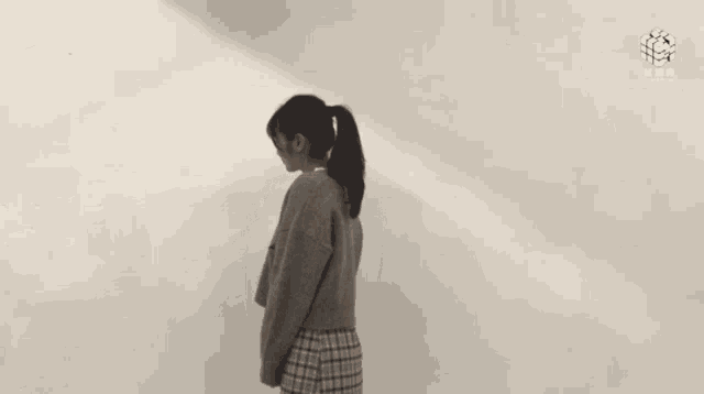 a woman is standing in front of a white wall wearing a sweater and a plaid skirt .
