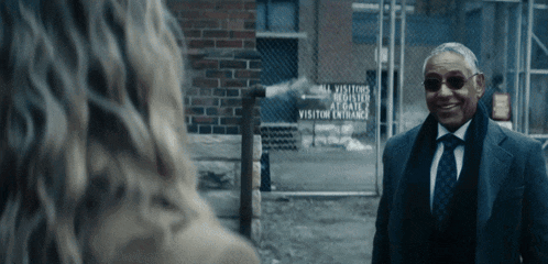 a man in a suit and tie is smiling in front of a sign that says visitor entrance