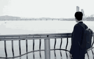 a man with a backpack is standing on a bridge overlooking a river .