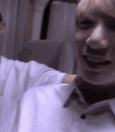 a man in a white shirt is laughing with his eyes closed while sitting in a chair .