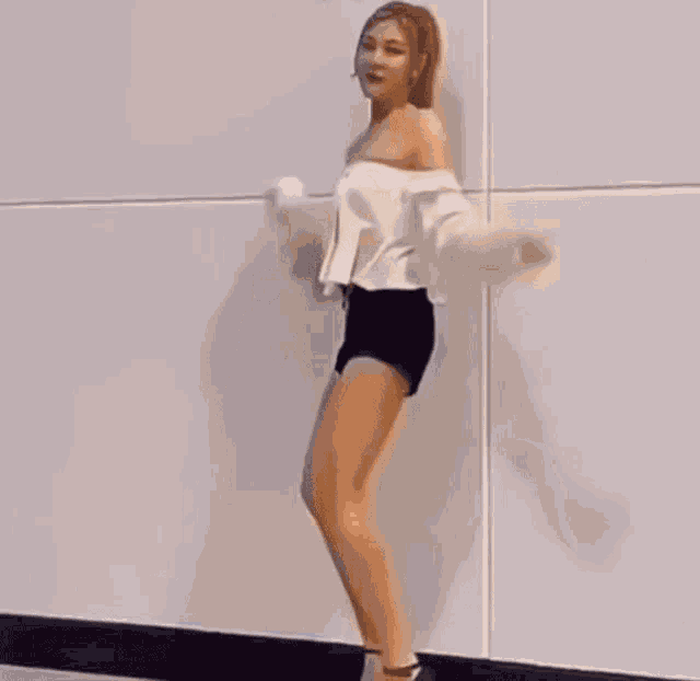 a woman in a white off the shoulder top and black shorts is dancing .
