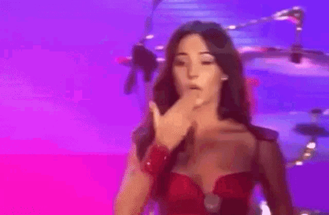 a woman in a red dress is singing into a microphone on a stage in front of a drum set .
