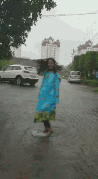 a woman wearing a blue raincoat is walking down a flooded street .