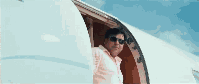 a man in a pink shirt and sunglasses is getting out of a plane .