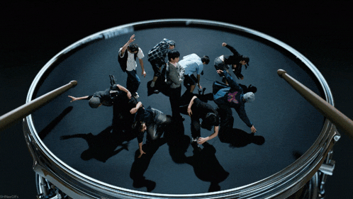 a group of people are dancing around a drum with a drum stick in the middle