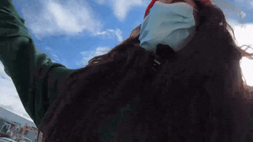 a woman wearing a face mask and a green sweater has her arms up in the air