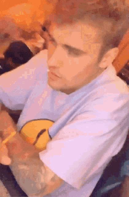 a man in a white shirt with a yellow smiley face on it is sitting at a table eating food .