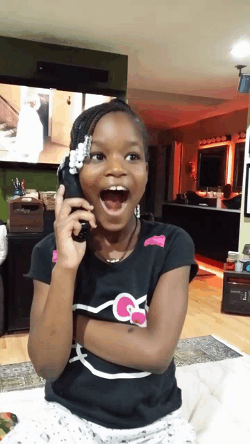 a little girl with a hello kitty shirt on is talking on a cell phone