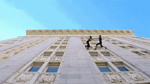two people climb up the side of a building with a blue sky in the background