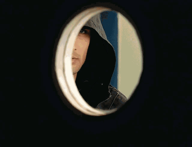 a man wearing a black hooded jacket is standing in front of a wall