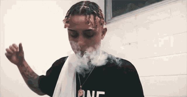 a man with braids is smoking a cigarette in a bathroom .