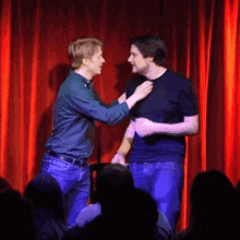 two men are standing on a stage in front of a red curtain