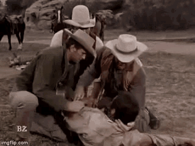 a group of men in cowboy hats are helping a man in a field .