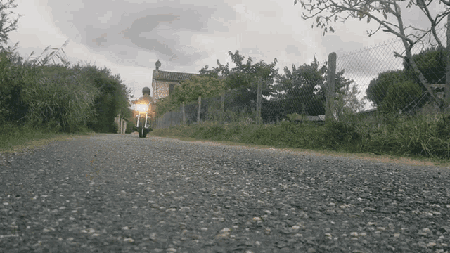 a person riding a motorcycle down a gravel road with a fence in the background