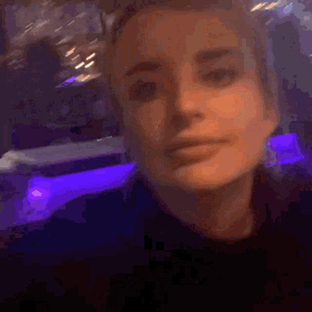 a close up of a woman 's face in a dark room with purple lights behind her