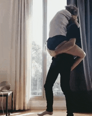 a man is carrying a woman in his arms in front of a window in a living room .