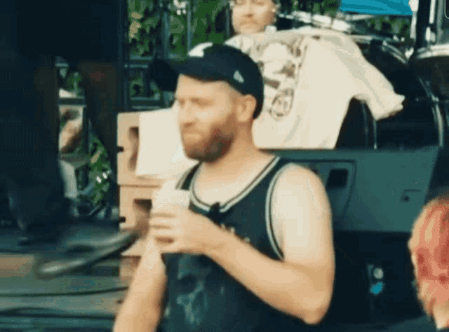 a man with a beard is holding a cup and wearing a black hat with the letter n on it