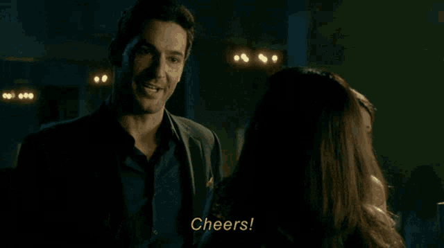 a man is holding a glass of whiskey and smiling while a woman says cheers