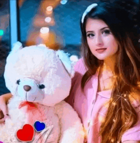 a woman in a pink shirt is holding a teddy bear with hearts on it .