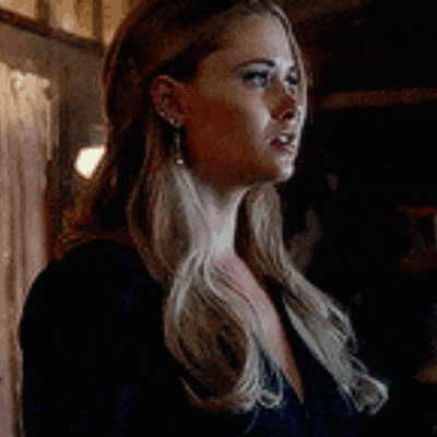 a woman with long blonde hair and earrings is standing in a dark room .